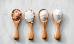 Various salt types in 4 wooden spoons on white marble.