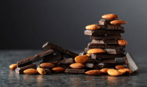 Broken dark chocolate bar with almond on a black background. Copy space.